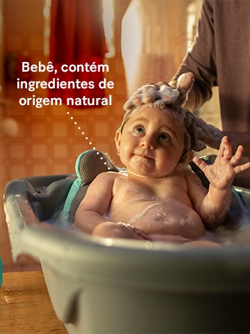 Bebê em banheira com pai lavando seu cabelo. "Bebê, contém ingredientes de origem natural."