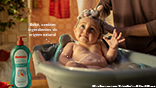 Bebê em banheira com pai lavando seu cabelo. "Bebê, contém ingredientes de origem natural."